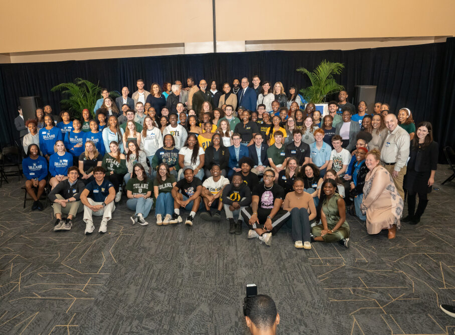 Large group photo of diverse college students, faculty and non-profit representatives gathered at the Unity Summit in New Orleans, February 2025. Participants are smiling and seated or standing in rows, with some wearing university shirts from Tulane and Dillard. The background includes potted plants and black curtains.