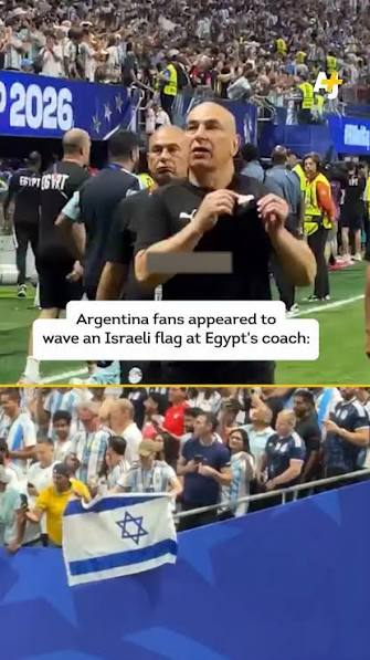 Split-screen image showing a soccer stadium during a match. The top panel shows Egypt's head coach standing on the sideline while looking toward the crowd. An on-screen caption reads: "Argentina fans appeared to wave an Israeli flag at Egypt's coach:" The bottom panel shows spectators in Argentina jerseys holding an Israeli flag over the front railing of the stands. A broadcast logo appears in the top-right corner.