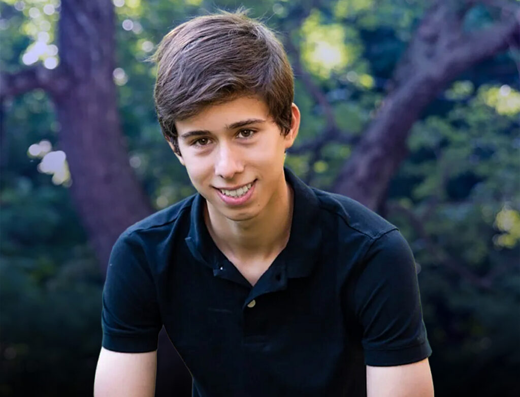 Austin Franco smiling outdoors in a black polo shirt, with trees and greenery in the background.