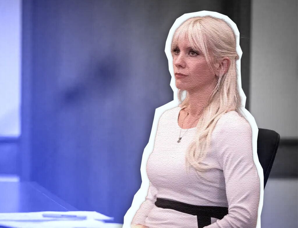 Shiloh Hendrix sits at a table in what appears to be a courtroom or hearing room. She is wearing a fitted white long-sleeve top and has straight, light-blonde hair with bangs. She faces slightly to her left with a serious, attentive expression. The image has been edited with a thick white outline around her figure, creating a cutout effect against a blurred background. A blue light flare or gradient fills the left side of the image, and papers and a pen are visible on the table in the foreground.