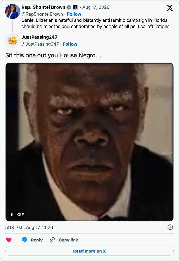 X user JustPassing247 directs a racist insult at Shontel Brown after her condemnation of Bilzerian’s antisemitic campaign, accompanied by a GIF of a stern-looking man.