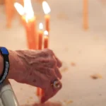 A hand wearing a Stand Up to Hate bracelet reaches toward lit candles at St. David Armenian Church.