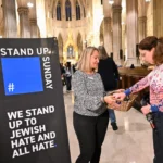 Two people stand with a basket beside a Stand Up Sunday banner at St. Patrick’s Cathedral in New York.